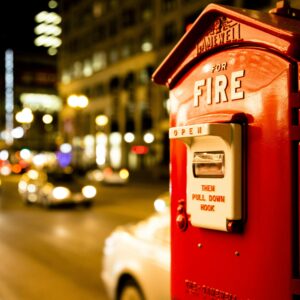 A classic red fire alarm box on a city street lit by car headlights at night.