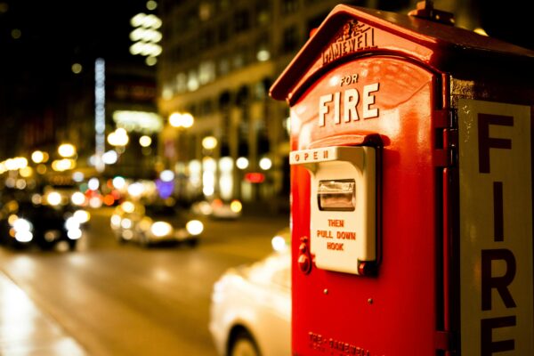 A classic red fire alarm box on a city street lit by car headlights at night.